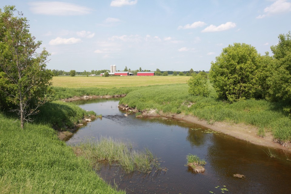 A farm is seen in the distance, with a pastoral river leading towards it.